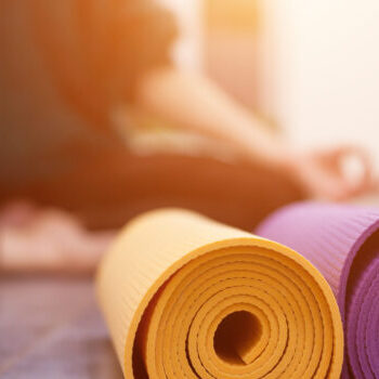 Closeup view of yoga mat and woman sitting in lotus pose on background. Yoga exercising in gym